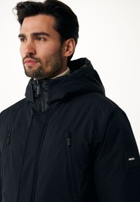 Černá zateplená bunda s vysokým límcem a odnímatelnou kapucí, která má dvě kapsy na zip na hrudi, elegantní design a nášivku s logem na rukávu.