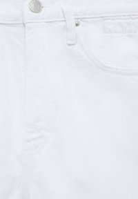 Gros plan d'un jean en denim blanc montrant la ceinture, le bouton en métal, la passants de ceinture et le détail de la poche avant.