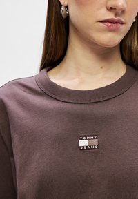 Brązowa bawełniana bluza z długim rękawem z przyszytą naszywką "TOMMY JEANS" z przodu. Okrągły dekolt i gładka faktura, z krótkimi rękawami.