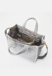 Saco de tecido cinza com exterior texturizado, logótipo bordado e interior com padrão. Apresenta ferragens douradas e uma alça destacável.