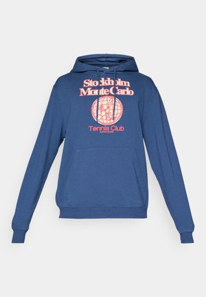 Blaue Kapuzenjacke mit Fronttasche, Kordelzügen und rotem Text "Stockholm Monte Carlo Tennis Club" über einem Globus-Graphic.
