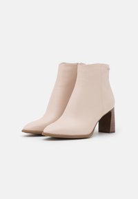 Botines beige confeccionados en cuero liso, con punta afilada y tacón medio de madera, con detalle de cremallera lateral.