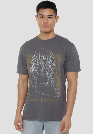Young man wearing gray "Game of Thrones" t-shirt featuring a distressed Iron Throne graphic, paired with light blue jeans.
