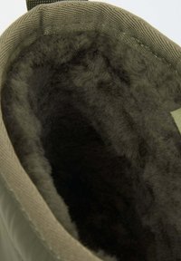 Groene stoffen laars met een zachte, donkere bontvoering en een gestructureerde buitenkant. Heeft een vlakke bovenkant en een stevige lus voor gemakkelijk hanteren.