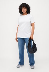 White cotton t-shirt, relaxed fit, short sleeves; paired with light blue jeans. Holding a black scrunchie-style handbag.