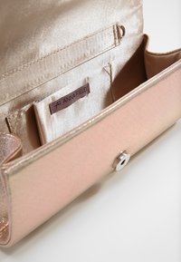 Rosa metallisk clutch-plånbok med slät yta, knäppstängning och innerfack. Varumärkesetikett synlig inuti. Satinfoder som reflekterar ljus.