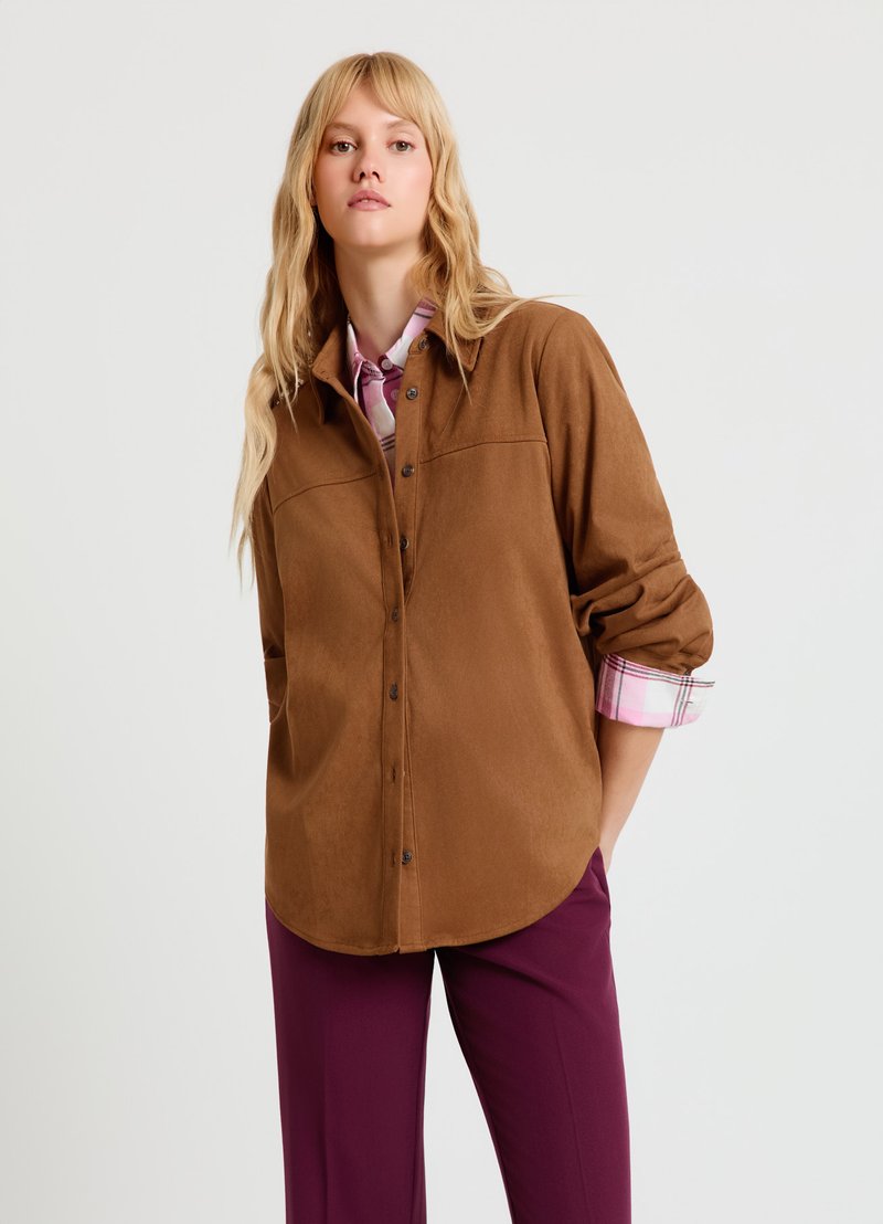 Chemise marron à boutons en tissu doux ressemblant à du daim, avec un col pointu et des poches poitrines. Les poignets sont doublés d'un tissu à carreaux rose contrastant.