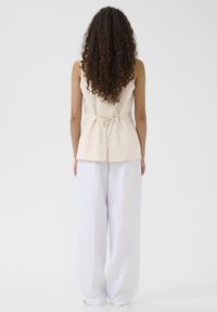 Beige linne-topp med en knytning baktill, kombinerad med löst sittande vita linnebyxor. Släta texturer, enkel design och minimalistisk stil.