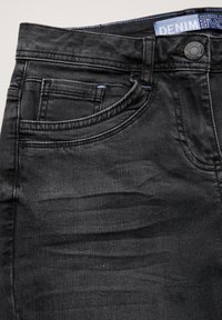 Jeans de mezclilla negra con una textura suave, que cuentan con un bolsillo frontal, detalles cosidos y un cierre de botón en la cintura.