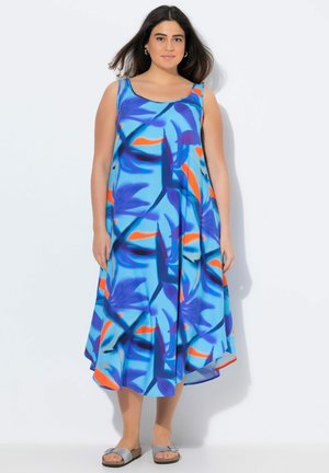 Vestido maxi azul con patrón floral abstracto en naranja y azul oscuro. Sin mangas, de corte holgado y con dobladillo fluido, combinado con sandalias grises.