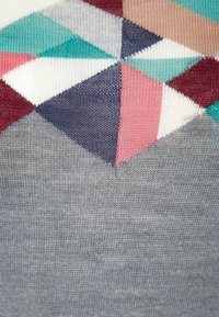 Tejido de punto con un patrón geométrico en varios colores: turquesa, blanco, burdeos y rosa, que se va desvaneciendo en una base gris sólida.