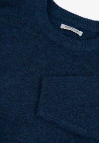 Navy blue neulepaita, jossa on pyöreä pääntie ja paikka tasku vasemmassa rinnassa. Pehmeä pinta, joka on hieman pörröinen.