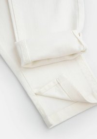 Biała tkanina dżinsowa ma złożone mankiety i skośne detale szwów. Gładka tekstura o ustrukturyzowanym kształcie, zwięzły i schludny design.