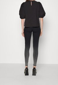 Top negro de manga abullonada con textura, abertura en la parte trasera del cuello, combinado con jeans skinny de ombré oscuro a claro, y zapatos de tacón cuadrado negros.