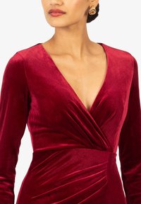 Tiefrotes Samtkleid mit einem tiefen V-Ausschnitt, langen Ärmeln und gerafftem Stoffdetail an der Taille. Besitzt eine glatte Textur und einen eleganten Fall.