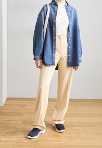 Denim shirt in blue with buttons, cream turtleneck, beige wide-leg pants, and navy sneakers with white soles, set on a wooden floor.