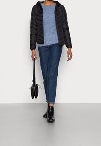 Černá péřová bunda s kapucí, světle modrý pletený svetr, džíny, černé kotníkové boty a malá černá kabelka.