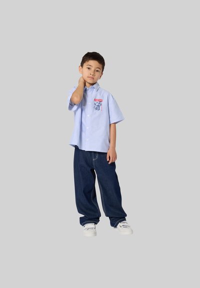 Blauw-wit gestreept shirt met korte mouwen en "KENZO" logo, gecombineerd met donkerblauwe wide-leg jeans en witte schoenen.