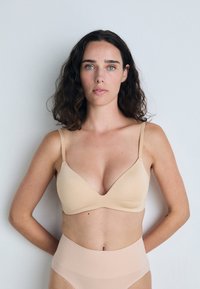 Nude-colored, seamless bra with a soft texture and thin straps, featuring a classic triangular shape that provides a smooth silhouette.