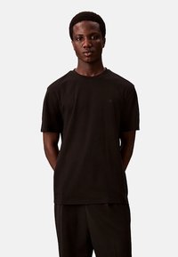 Zwarte katoenen t-shirt met korte mouwen. Ronde hals, reguliere pasvorm, met een klein logo op de linkerkant van de borst. Effen kleur, gladde textuur.