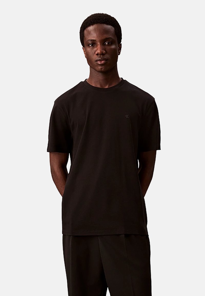 Zwarte katoenen t-shirt met korte mouwen. Ronde hals, reguliere pasvorm, met een klein logo op de linkerkant van de borst. Effen kleur, gladde textuur.