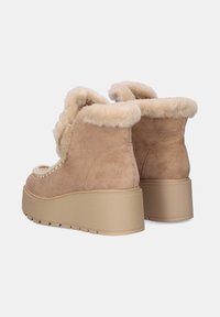 Botas de ante marrón claro hasta el tobillo con forro de piel sintética beige, suela plataforma gruesa y costuras decorativas en la parte superior. Diseño de puntera redondeada.