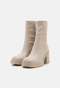Beige Leder-Ankle-Boots mit einem eng anliegenden Design, Blockabsatz und sichtbaren Stickdetails. Glatte Textur und abgerundete Zehen.