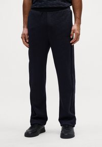 Pantaloni da uomo in tessuto testurizzato con vita elasticizzata di colore blu navy. Presentano un delicato motivo geometrico e tasche laterali, abbinati a sneakers nere.