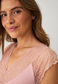 Blush-pink Oberteil mit Spitzenausschnitt und floralen Mustern sowie einem weichen Stoff. Das Design ist tailliert mit einem V-Ausschnitt.