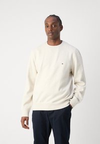 Cremfarbener Sweatshirt aus Fleece-Material, mit Rundhalsausschnitt und gerippten Bündchen, sowie einem kleinen Logo auf der linken Brust.