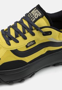 Vans sportiniai bateliai su geltonu tekstiliniu viršumi, tamsiai pilkomis raišteliais, juodais akcentais ir tekstūruotu padu su grioveliais sukibimui.