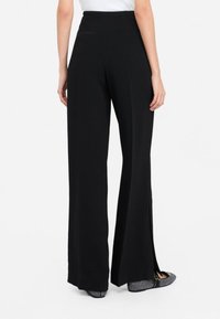 Pantalones de pierna ancha negros, hechos de una tela suave, con una cintura alta y cortes laterales. La parte de atrás incluye un pequeño detalle de bolsillo.