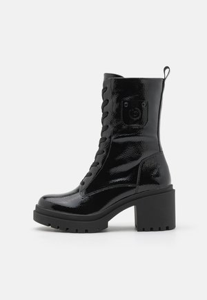 Black patent leather ankle boot with a chunky heel, lace-up front, and rounded toe. Features distinct treaded sole and a heel accent.