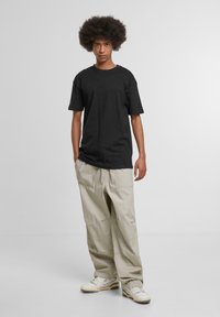 Black cotton t-shirt with a relaxed fit, paired with light beige cargo pants, featuring multiple pockets and a slightly tapered design.
