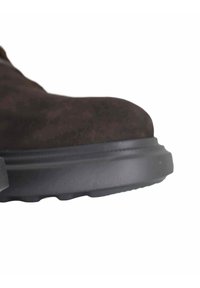 Stivaletto alla caviglia in camoscio marrone con punta arrotondata, suola in gomma nera testurizzata e cuciture sottili lungo il bordo.