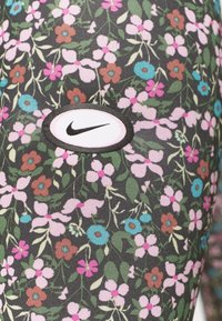 Leggings florales con un fondo negro, que presentan flores en tonos rosa, azul y marrón. Un logo ovalado de Nike está bordado en blanco y negro.