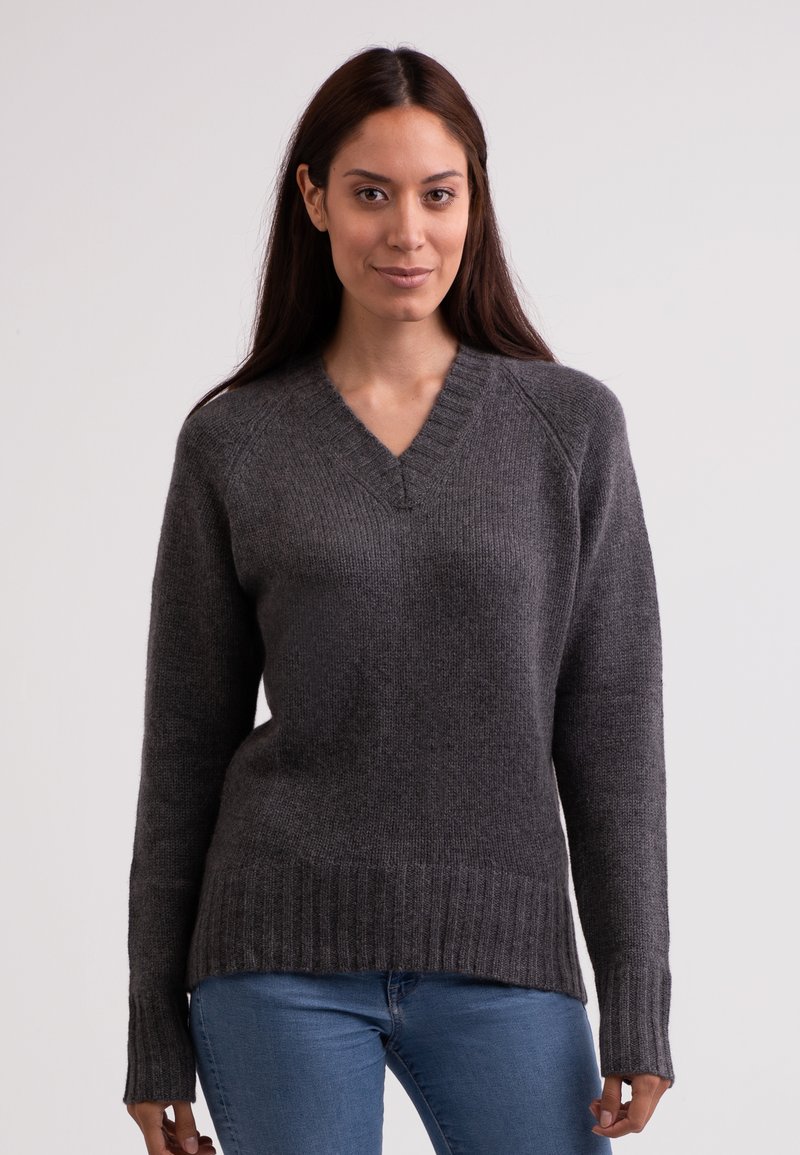 Maglione grigio lavorato a maglia con scollo a V, polsini e orlo a coste. Presenta una texture morbida e una vestibilità leggermente rilassata, indossato sopra un paio di jeans blu.