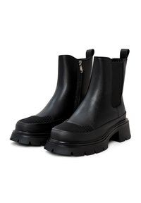 Bottines noires à cheville avec une finition lisse et brillante. Présentent des semelles épaisses, des accents côtelés, une fermeture éclair latérale et des panneaux élastiques pour un enfilage facile.