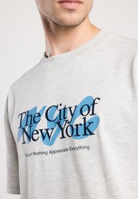 Gray cotton t-shirt featuring "The City of New York" in blue and navy text with a light blue accent, round neck, and short sleeves.