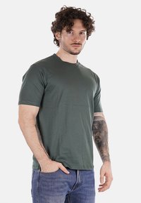 T-shirt verde a maniche corte in morbido cotone, con scollo rotondo e vestibilità rilassata, indossato con jeans blu.