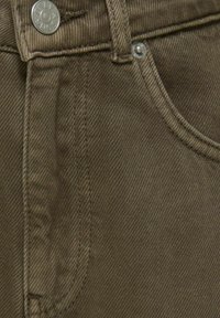 Brunt denim stof med et subtilt sildbenmønster, med en sølvmetal knap og kontrasterende syninger langs sømmene og lommerne.