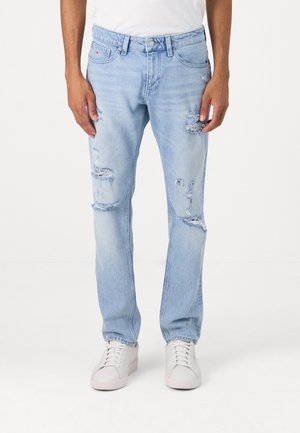 Light blue distressed jeans worn with white sneakers and a white shirt, shown from waist to feet on a plain background.