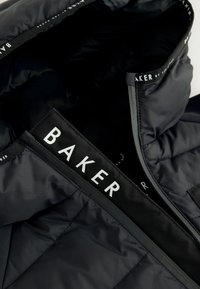 Czarna pikowana kurtka z wysokim kołnierzem, z zamkiem błyskawicznym z przodu oraz białym logo "BAKER" na kołnierzu i wewnętrznej metce. Miękka struktura.