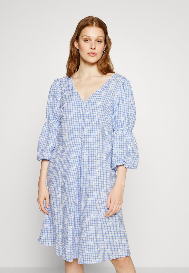 Vestido xadrez azul e branco com mangas bufantes, decote em V, padrões florais e uma silhueta descontraída. Tecido de algodão leve.