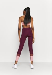 Urheiluvaatteet, joissa on vaaleanpunainen urheilu-toppi ja burgundinpunaiset legginssit, joissa on vaaleanpunaiset verkkokohdat nilkoissa. Sileä pinta, tiukka muotoilu.