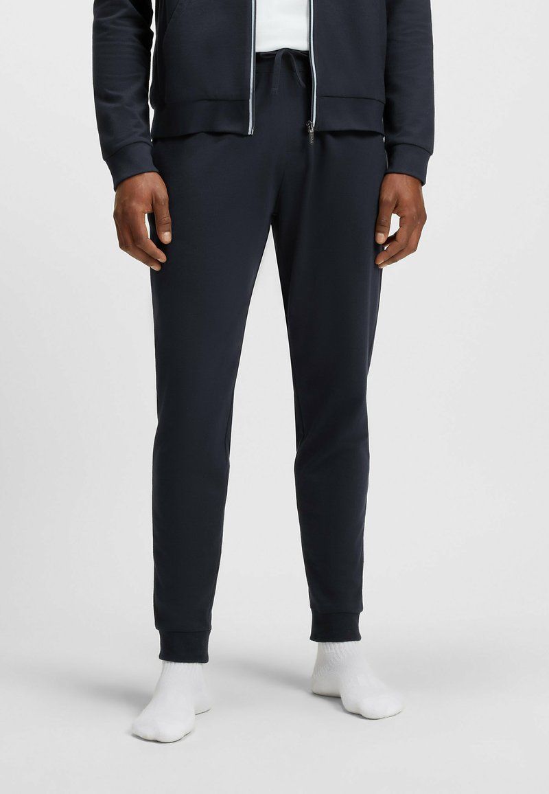 Marineblauwe joggers van zacht materiaal, met een tailleband met trekkoord, ribgebreide boorden en een slank silhouet. Vervormde ontwerp voor extra comfort.
