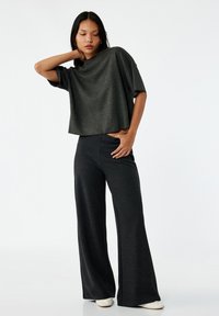 Camiseta corta gris oscuro con mangas cortas y anchas, combinada con pantalones sueltos gris oscuro, ambos hechos de una tela suave y texturizada.