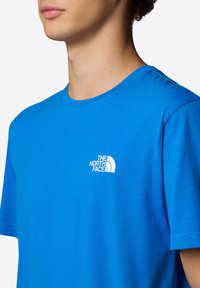 Blå bomulls t-shirt med kort ärm och en vit "The North Face"-logotyp på vänster bröst, rund halsringning och normal passform.