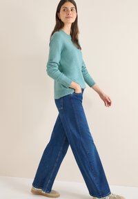 Lichtblauwe gebreide trui met lange mouwen, gecombineerd met donkerblauwe wijde jeans. De outfit wordt aangevuld met beige schoenen.