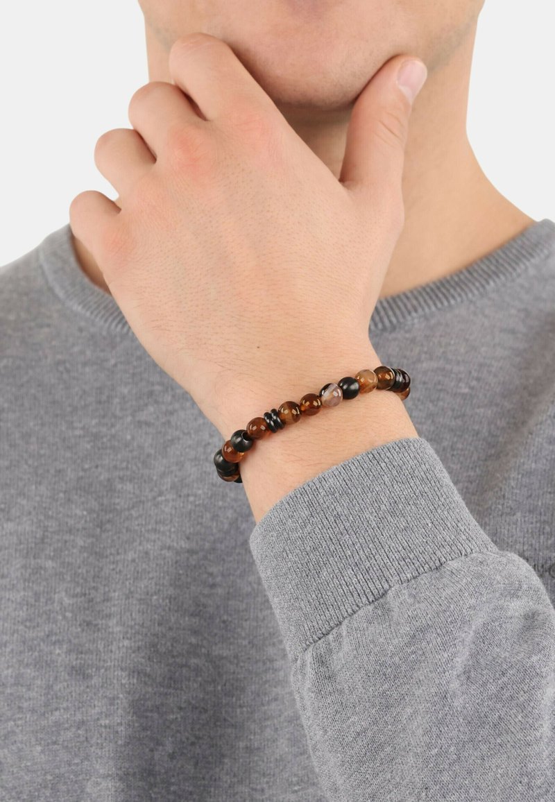 Pulsera de cuentas con piedras de ámbar y negras, presentando patrones alternos y un diseño flexible, llevada en una muñeca con un suéter gris.